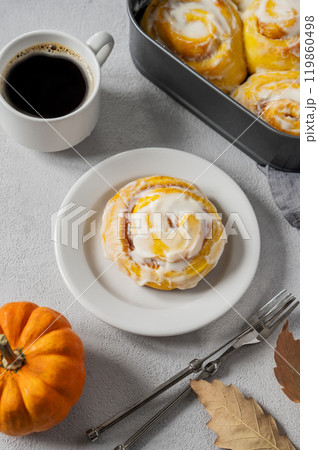 Flat lay of sweet pumpkin rolls with creamy glaze and cinnamon on a plate on a light background  119860498