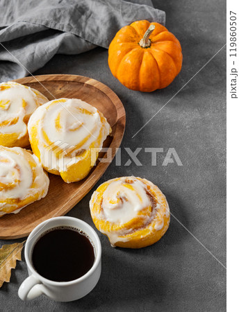 Pumpkin rolls with creamy glaze and cinnamon on a wooden plate on a dark  background Pumpkin rolls with creamy glaze and cinnamon on a wooden plate on a dark  background 119860507