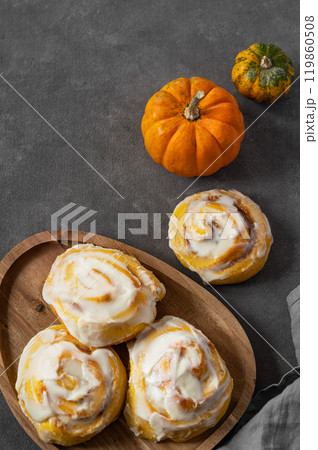 Pumpkin rolls with creamy glaze and cinnamon on a wooden plate on a dark  background. 119860508