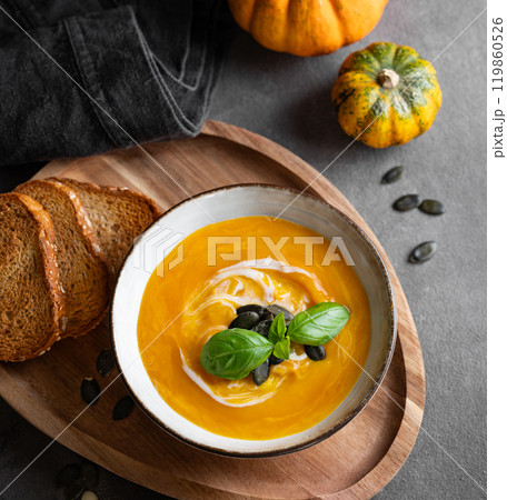Pumpkin soup with cream, basil and seeds on a wooden board with fried bread on a dark background Pumpkin soup with cream, basil and seeds on a wooden board with fried bread on a dark background 119860526