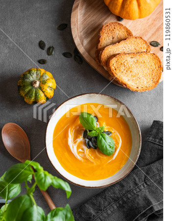 Homemade pumpkin soup with cream, basil and seeds on a dark background with fresh pumpkins 119860531
