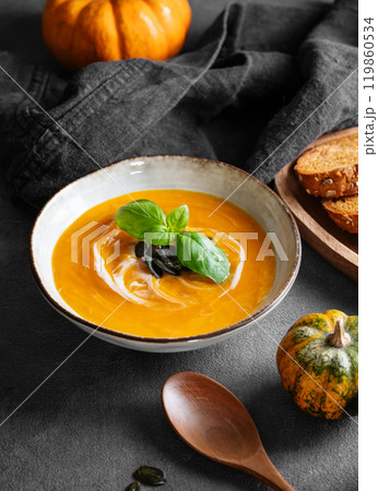 Pumpkin soup with cream, basil and seeds on a dark background with fresh pumpkins, fried bread 119860534
