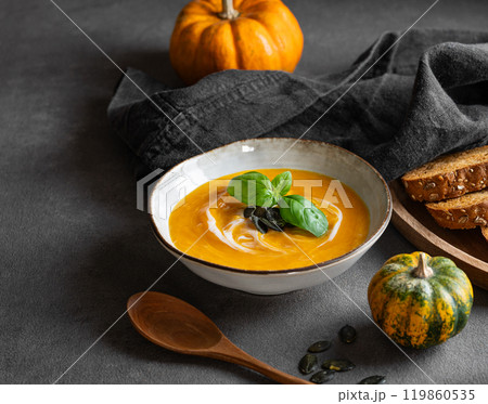 Pumpkin soup with cream, basil and seeds on a dark background with fresh pumpkins, fried bread 119860535