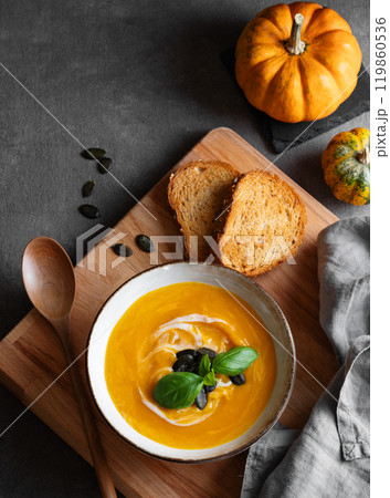 Pumpkin soup with cream, basil and seeds on a wooden board with fried bread and spoon Pumpkin soup with cream, basil and seeds on a wooden board with fried bread and spoon 119860536
