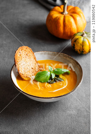 Homemade pumpkin soup with cream, basil and seeds on a dark background with bread and fresh pumpkins Homemade pumpkin soup with cream, basil and seeds on a dark background with bread and fresh pumpkins 119860542