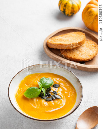 Pumpkin soup with cream, basil and seeds on a light background with bread and spoon. Pumpkin soup with cream, basil and seeds on a light background with bread and spoon. 119860548