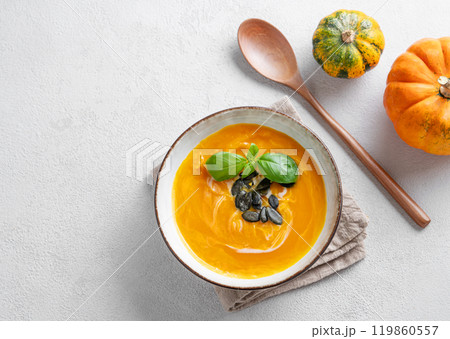 Flat lay of pumpkin soup with cream, basil and seeds on a light background with fresh pumpkins 119860557