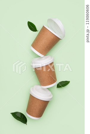Three brown paper coffee cups with white lids on green background with leaves. Three brown paper coffee cups with white lids on green background with leaves. 119860606