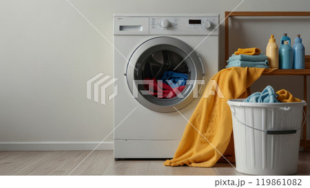 The washing machine sits prominently surrounded by various detergent bottles and a wicker laundry basket, emphasizing organization and cleanliness. 119861082