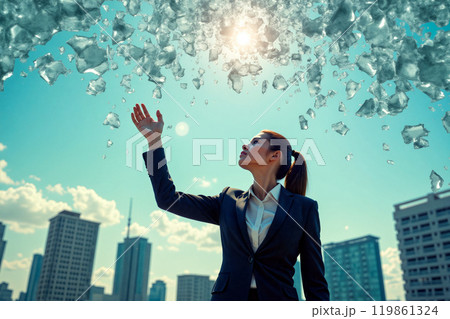 Businesswoman reaching for a shard of glass against a backdrop of skyscrapers and a bright blue sky 119861324