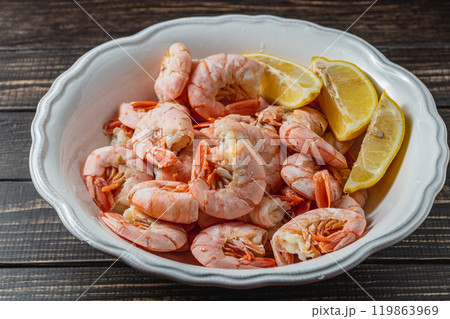 Boiled king prawns in deep bowl with lemon close up view on dark table 119863969