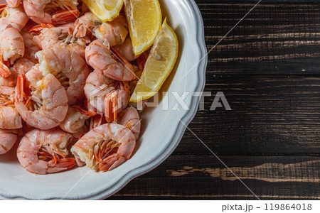 Boiled king prawns in deep bowl with lemon close up view on dark table 119864018