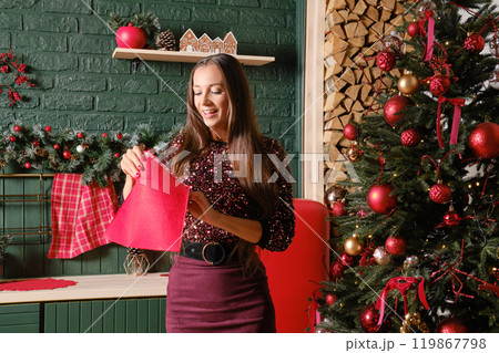 A woman opens red envelope, standing next to a beautifully decorated Christmas tree 119867798