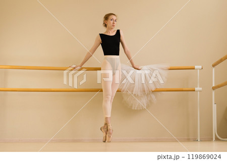 Ballet dancer standing on pointe at barre, holding tutu 119869024