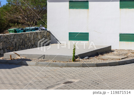A concrete slab rests quietly at the corner of a quiet street, surrounded by nature\'s touch, hinting at upcoming construction on a sunny day 119871514