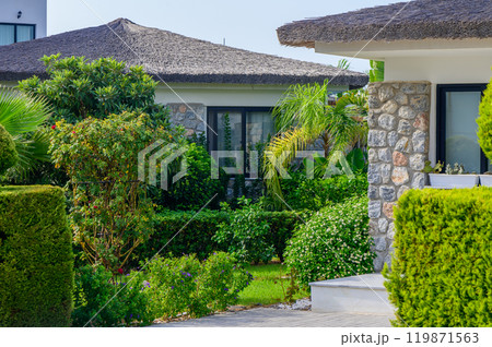 Charming villa with lush greenery and tropical plants under a bright blue sky in a tranquil resort setting 119871563