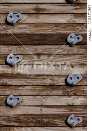 Climbing wall with textured holds against wooden backdrop on a sunny day in an outdoor fitness park 119871566
