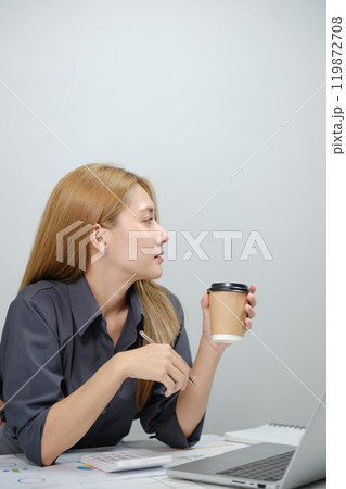 A woman is sitting at a desk with a laptop and a cup of coffee A woman is sitting at a desk with a laptop and a cup of coffee 119872708