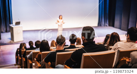 Business and entrepreneurship symposium. Female speaker giving a talk at business meeting. Audience in conference hall. Rear view of unrecognized participant in audience. Business and entrepreneurship symposium. Female speaker giving a talk at business meeting. Audience in conference hall. Rear view of unrecognized participant in audience. 119873324