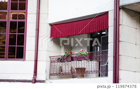 Cozy balcony with red awning and flower pots on a building facade. Cozy balcony with red awning and flower pots on a building facade. 119874378