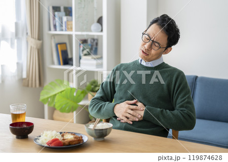 食卓で胃の辺りに手をあてるアラフォーの男性 食卓で胃の辺りに手をあてるアラフォーの男性 119874628