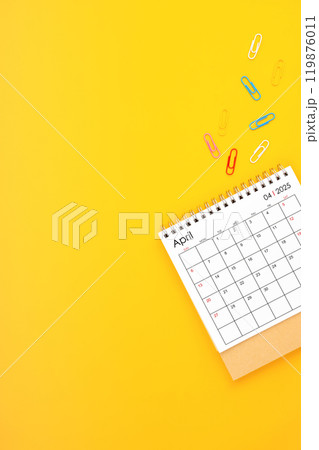April 2025 desk calendar and paper clips on yellow background. Position with copy space. 119876011