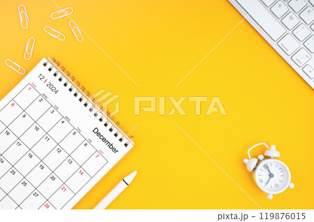 December 2024, Monthly desk calendar for 2024 year and alarm clock with paper clips on yellow color background. 119876015