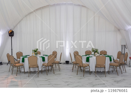 Wine glasses, silver tableware and green napkins on round tables covered with white tablecloth. Wine glasses, silver tableware and green napkins on round tables covered with white tablecloth. 119876081