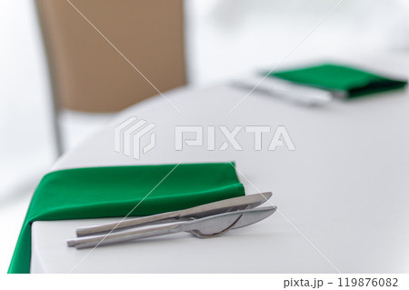 Close up of wine glasses, silver tableware and green napkins on round tables covered with white tablecloth. Close up of wine glasses, silver tableware and green napkins on round tables covered with white tablecloth. 119876082