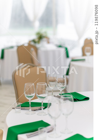 Close up of wine glasses, silver tableware and green napkins on round tables covered with white tablecloth. Close up of wine glasses, silver tableware and green napkins on round tables covered with white tablecloth. 119876098