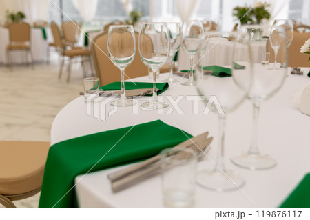 Close up of wine glasses, silver tableware and green napkins on round tables covered with white tablecloth. Close up of wine glasses, silver tableware and green napkins on round tables covered with white tablecloth. 119876117