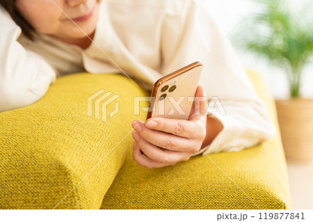 ソファに寝そべってスマホを見るミドル〜シニア女性 119877841