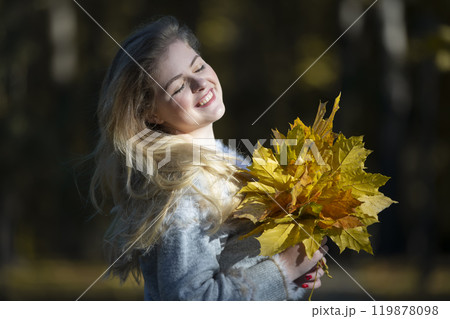 Beautiful young woman in an autumn park with a bouquet of maple leaves. 119878098