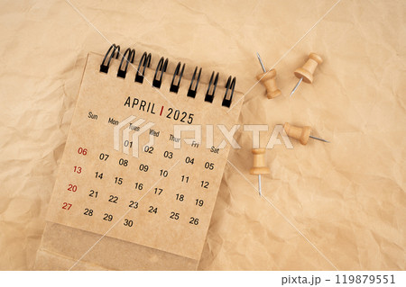 April 2025 desk calendar with wooden thumbtack on brown crumpled paper background. 119879551