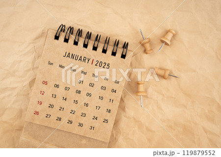 January 2025 desk calendar with wooden thumbtack on brown crumpled paper background. 119879552
