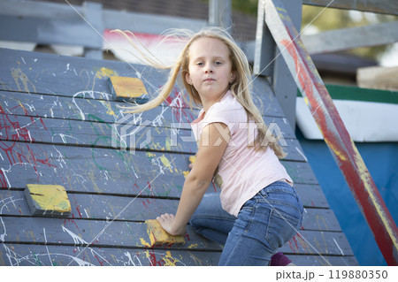 A little girl is climbing a rock climbing wall. The child plays on the children's slide. 119880350