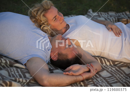 A beautiful middle-aged couple in love lies on the grass. A man and a woman are resting in nature. A beautiful middle-aged couple in love lies on the grass. A man and a woman are resting in nature. 119880375