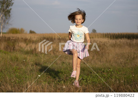 Beautiful little girl runs in the summer field. The child plays in the meadow. 119880422