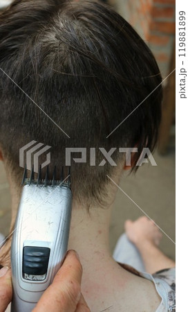 vertical photo of young man cutting hair with electric trimmer, close-up, hand with hair clipper cutting hair on back of teenager's head vertical photo of young man cutting hair with electric trimmer, close-up, hand with hair clipper cutting hair on back of teenager's head 119881899