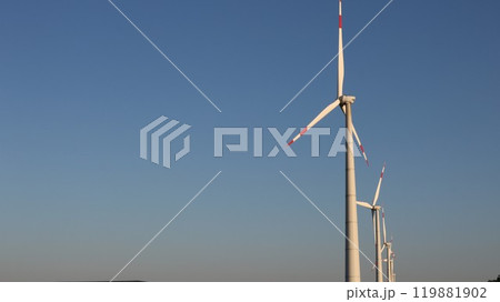 row of wind generators standing on the right side of the banner with blue background of light sky, windmills with large blades on the background of high clear sky with copy space row of wind generators standing on the right side of the banner with blue background of light sky, windmills with large blades on the background of high clear sky with copy space 119881902