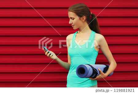 Fitness young woman with smartphone and yoga mat on red background 119881921