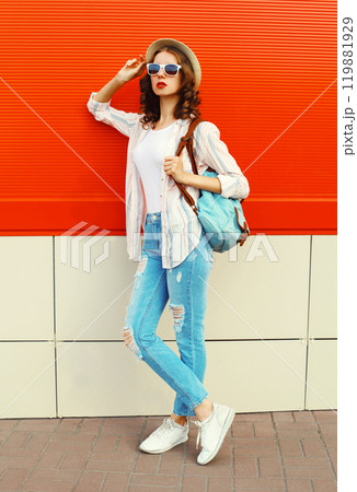 Young woman model posing wearing a casual, summer straw round hat on city street over red background Young woman model posing wearing a casual, summer straw round hat on city street over red background 119881929