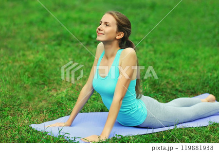 Fitness woman doing yoga exercises back stretching on a mat on the grass in summer park 119881938