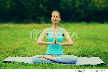 Young woman doing yoga exercises on a mat on the grass in summer park 119881943