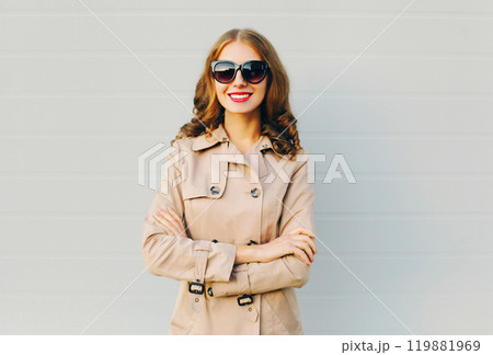 Fashion portrait pretty smiling woman wearing a coat and black sunglasses over grey background Fashion portrait pretty smiling woman wearing a coat and black sunglasses over grey background 119881969