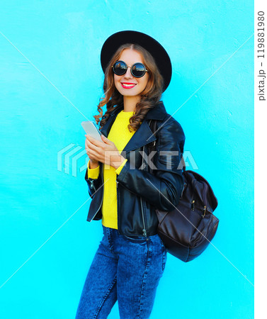 portrait young woman using smartphone wearing a black rock style clothes on colorful blue background 119881980