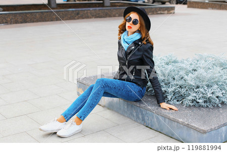 Fashion young woman posing in black rock jacket, hat at city park Fashion young woman posing in black rock jacket, hat at city park 119881994