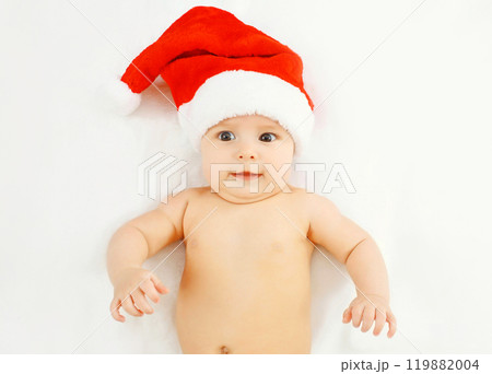 Christmas, family concept - cute baby in red santa hat lying on white bed home Christmas, family concept - cute baby in red santa hat lying on white bed home 119882004