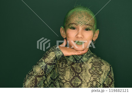 A beautiful adorable girl with painted green snake skin on her face shows off her makeup 119882121