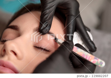 Beautician shaping eyebrows of client with tweezers in beauty salon 119882207